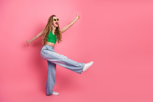 Cheerful young woman in vibrant green top and jeans having fun against pink background, expressing joy and energy