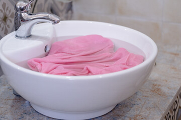 Close up of soaking pink cloth in a white sink. The setting a bathroom with simple decor. Concept of daily stains on clothes