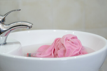 Close up of soaking pink cloth in a white sink. The setting a bathroom with simple decor. Concept...