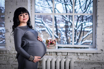 Pregnant woman stands at the window in the gray dress