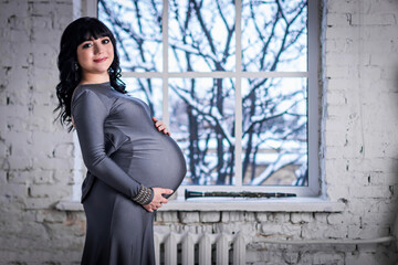Pregnant woman stands at the window in the gray dress