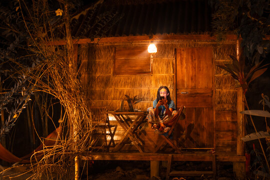 Young caucasian hipster woman sit use smartphone outside at night freelancing work, write travel blog or browse internet search, work online while traveling in southeast asia tropical islands - Powered by Adobe