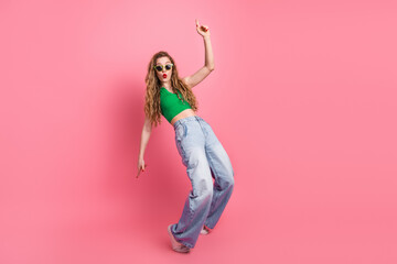 Stylish young woman in trendy outfit posing with playful energy against a vibrant pink background,...