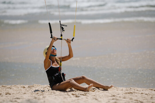Woman learning kitesurfing on sandy beach, sitting with control bar during beginner training. Wearing helmet and sunglasses. First lesson.