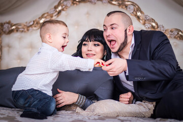 Dad and mom play with a son on the bed