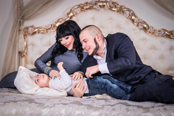 Happy young family in the bedroom. The father tickles his two-year-old son, the pregnant mother...
