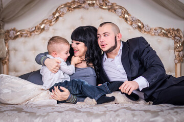 Dad and mom play with a son on the bed