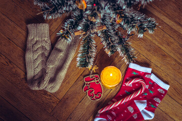 A candle is burning under the Christmas tree, near are cookies, candy, wool socks and mittens