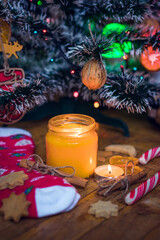 A candle is burning under the Christmas tree, near are cookies, candy, wool socks and mittens