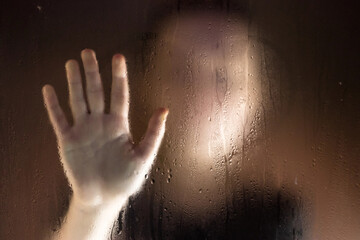 Girl outside window draws finger heart at wet glass. Girls out focus.