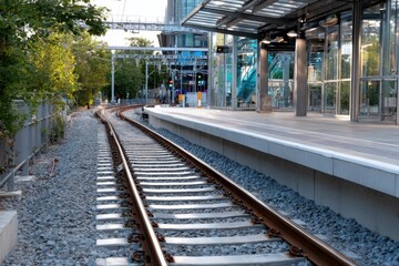 This image captures the perspective view of train tracks leading towards a modern urban station, showcasing the blend of nature and infrastructure in a metropolitan setting.