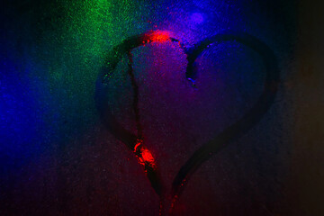 Heart drawn on wet glass. The lights of the night city through the wet glass.