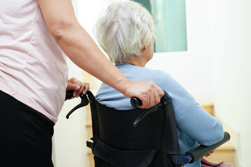 Caregiver help Asian elderly woman disability patient sitting on wheelchair in hospital.