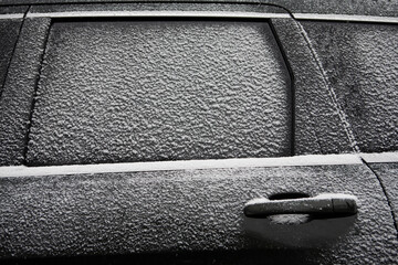 Close-up of car window and door covered with snow