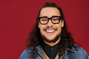 Confident young man in a denim jacket smiles against a vibrant red background