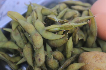 Boiled edamame is placed in a container and will be processed into a fruit salad.