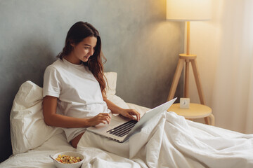 Young Woman Working on Laptop in Bed with Breakfast and Cozy Lighting