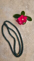 A long necklace of natural green jade with a flower beside it, isolated on a beige background.