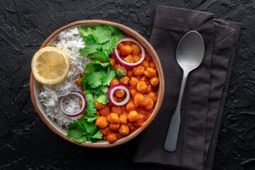 Chana masala, chickpea curry, traditional Indian dish, overhead flat lay shot with a spoon on a black background