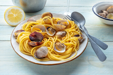 Vongole clams with spaghetti pasta, with lemon, with a wine glass, on a rustic wooden table