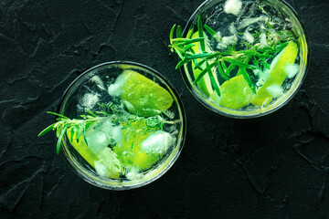 Gin tonic, top shot with rosemary and lime. Fresh summer cocktail with ice, on a black background