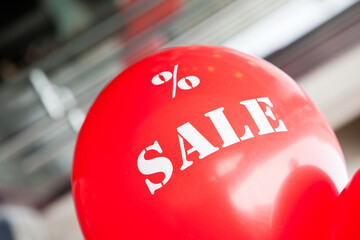 Sale concept. A red balloon with the text "% SALE" in front of a blurred shop background.