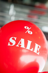 Sale concept. A red balloon with the text "% SALE" in front of a blurred shop background.