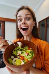 Excited young woman holding a bowl of fresh salad, showcasing healthy eating habits in a modern...