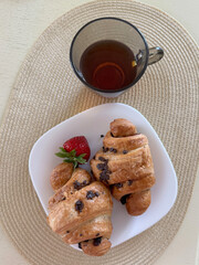 cozy breakfast setup with chocolate croissants, strawberry, and tea in a glass cup on a woven placemat.