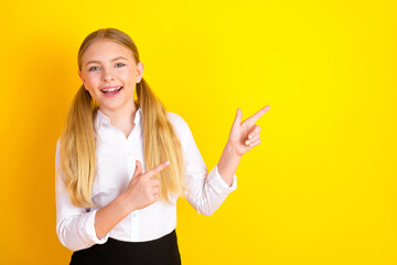 Cheerful schoolgirl pointing with enthusiasm against a vibrant yellow background, representing...
