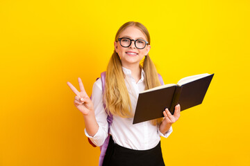 Smiling schoolgirl holding a book against a colorful yellow background showcasing learning and...