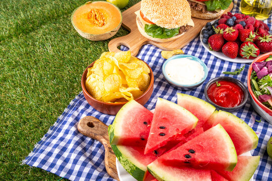 Summer picnic or BBQ brunch or lunch background, tasty barbecue table with hamburgers, salads, fruits, watermelon, sauces and snacks. Summer family and friends gathering picnic foods, copy space