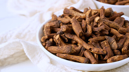 closeup macro pile of dry dandelion root herb for loose tea in bowl on white table background with copy space
