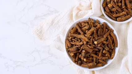 flat lay pile of dry dandelion root herb for loose tea in bowl on white table background with copy space
