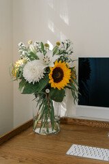 Minimalistic workspace with computer, keyboard and vase with summer flowers, illuminated by natural light. Wooden desk, linen curtains, vintage style room interior	