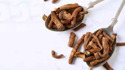 closeup pile of dry dandelion root herb for loose tea in metal spoon on white table background with copy space