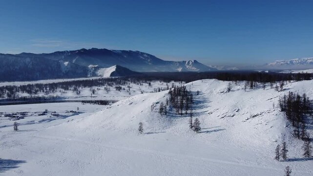 Drone footage of snowy mountains, valleys, and forests in Ust-Koksa, Altai Republic, Russia, under clear skies, showing the remote region&rsquo;s beauty during winter.