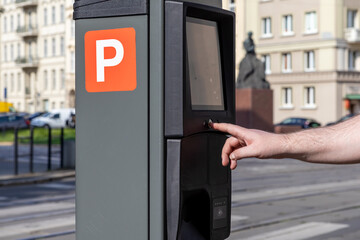 Human hand operates a modern city parking meter displaying an orange P sign for street payment,...