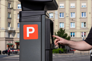 A person's hand operates a modern parking meter, featuring a prominent 'P' symbol, for efficient...