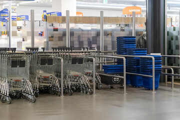 Neatly lined empty metal shopping carts and blue plastic baskets are ready for customer use within...