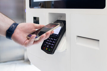 Hand using smartphone for Card Payment at a self-service terminal, highlighting modern digital...