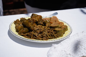 A traditional Cretan plate features vine leaves stuffed with wheat, tender wild greens, zucchini slices, and root vegetables under the sunlight in an outdoor courtyard.