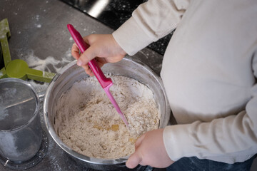 Child mixing dough with pink spatula in metal bowl