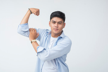 Young Filipino man in casual button-up flexes his biceps with a proud, strong, and confident facial...