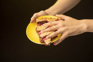 A beautifully layered slice of pie on a yellow plate is shown, held delicately by hands, inviting...