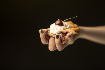 A close-up shot of a hand holding a slice of pie adorned with whipped cream and a cherry, illustrating the delicious textures and the joy of savoring culinary delights.