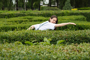 A person with long hair wearing a casual outfit explores a maze made of neatly trimmed hedges. The...