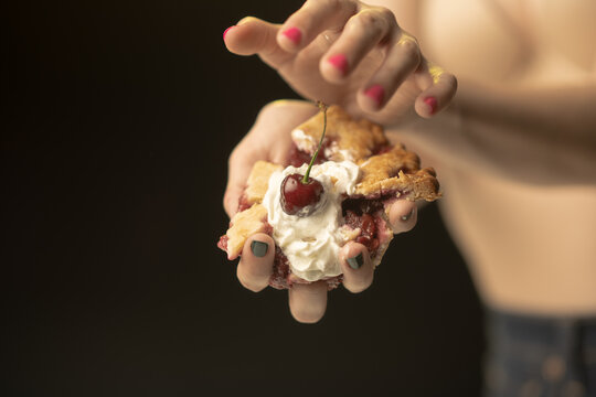 This captivating image showcases a hand presenting a slice of pie, topped with cream and a cherry. The focus on color and texture creates a unique visual appeal that entices viewers.