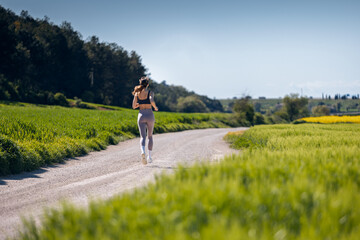 Obraz premium Back view of sporty woman running through the countryside
