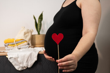 Pregnant woman holding red heart shape and feel love for unborn baby in belly. Awaiting for baby. Concept of maternity and pregnancy care